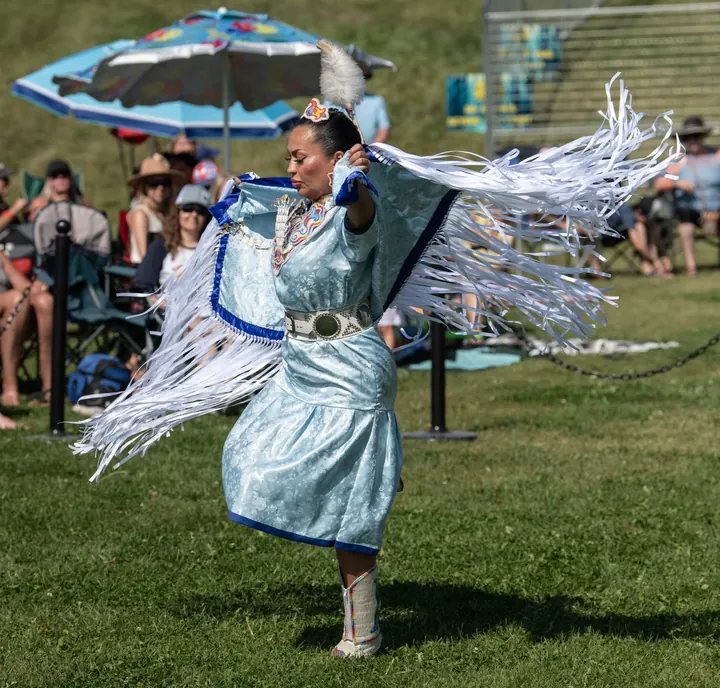 An Indigenous dancer in regalia performing on the field in 2025
